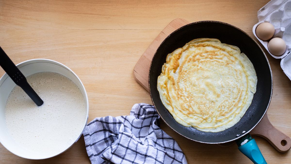 Crêpe en cours de cuisson dans une poêle avec pâte et œufs à proximité, comparatif crêpe maison et food truck