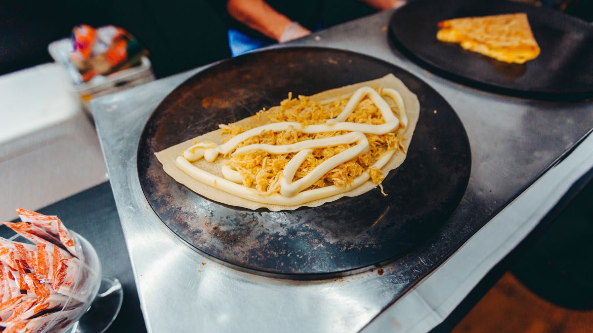 Galette de sarrasin garnie d'ingrédients savoureux en cours de cuisson sur une plaque chaude